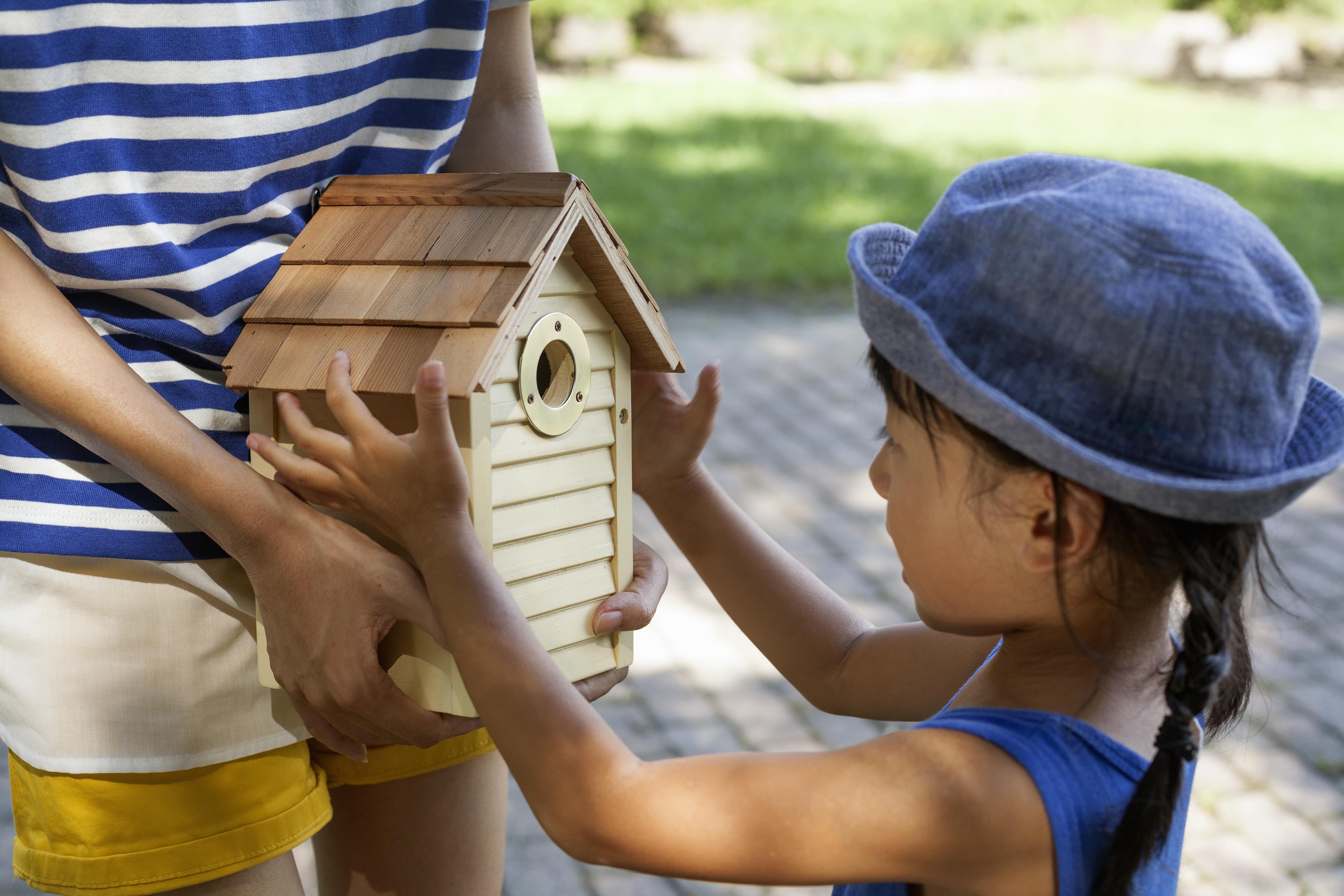 A young girl holding a DIY wooden birdhouse with her father.